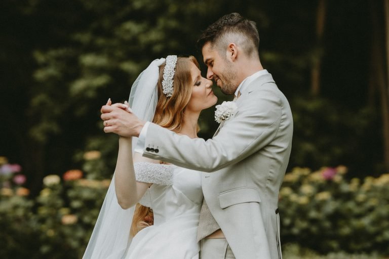 A bride and groom share a tender moment, holding hands and smiling during their first dance outdoors.